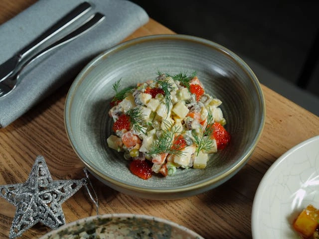 Kulhollinen maalaisperunasalaattia on pöydällä lautasen vieressä luoden viihtyisän ateria-asetelman.